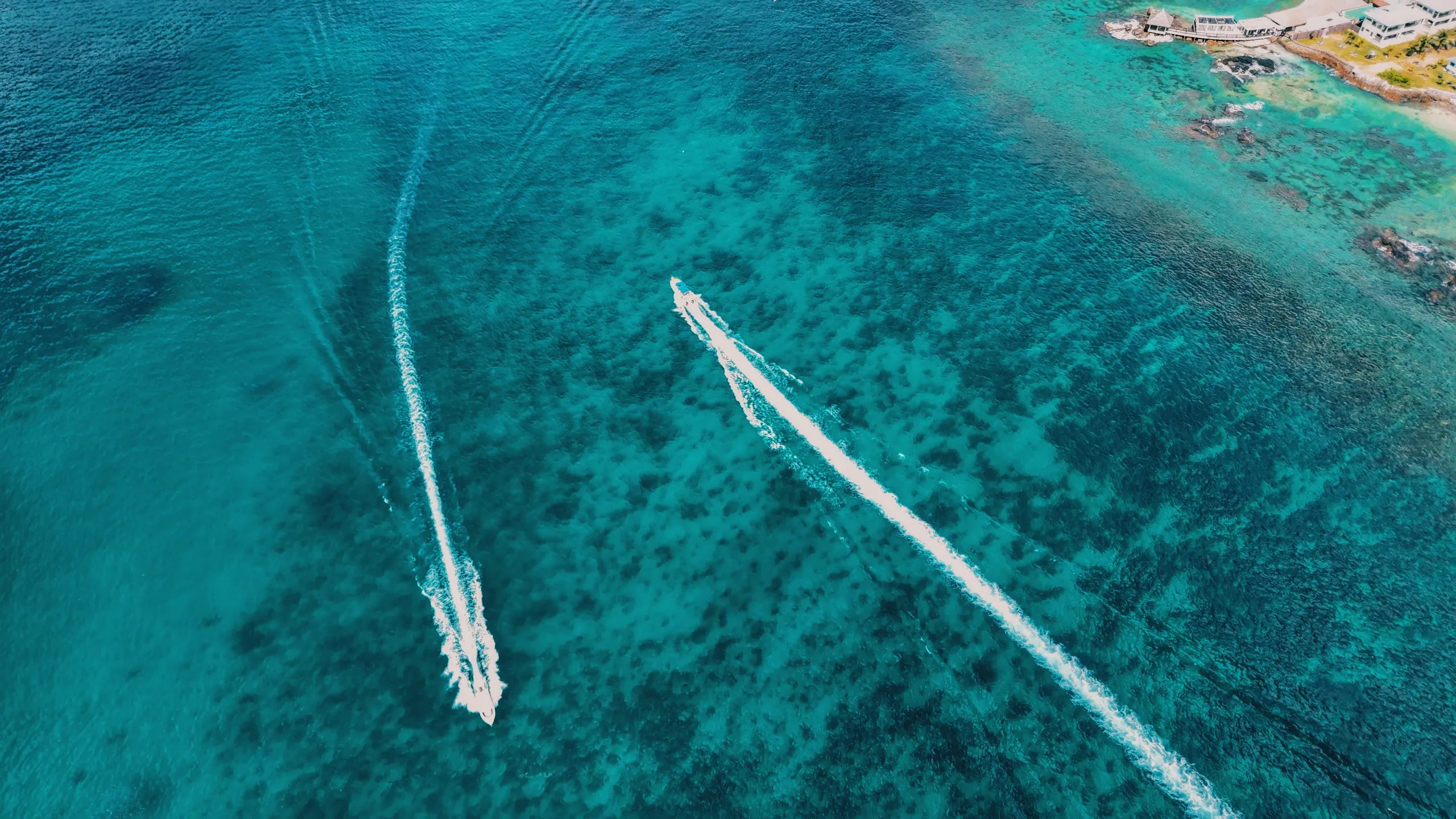 Two boats cutting wakes across turquoise shallows, seen from above